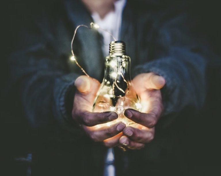 A leader wearing a suit holding an illuminated lightbulb, representing clarity in uncertain times or the inspiration to publish a leadership book in times of uncertainty.